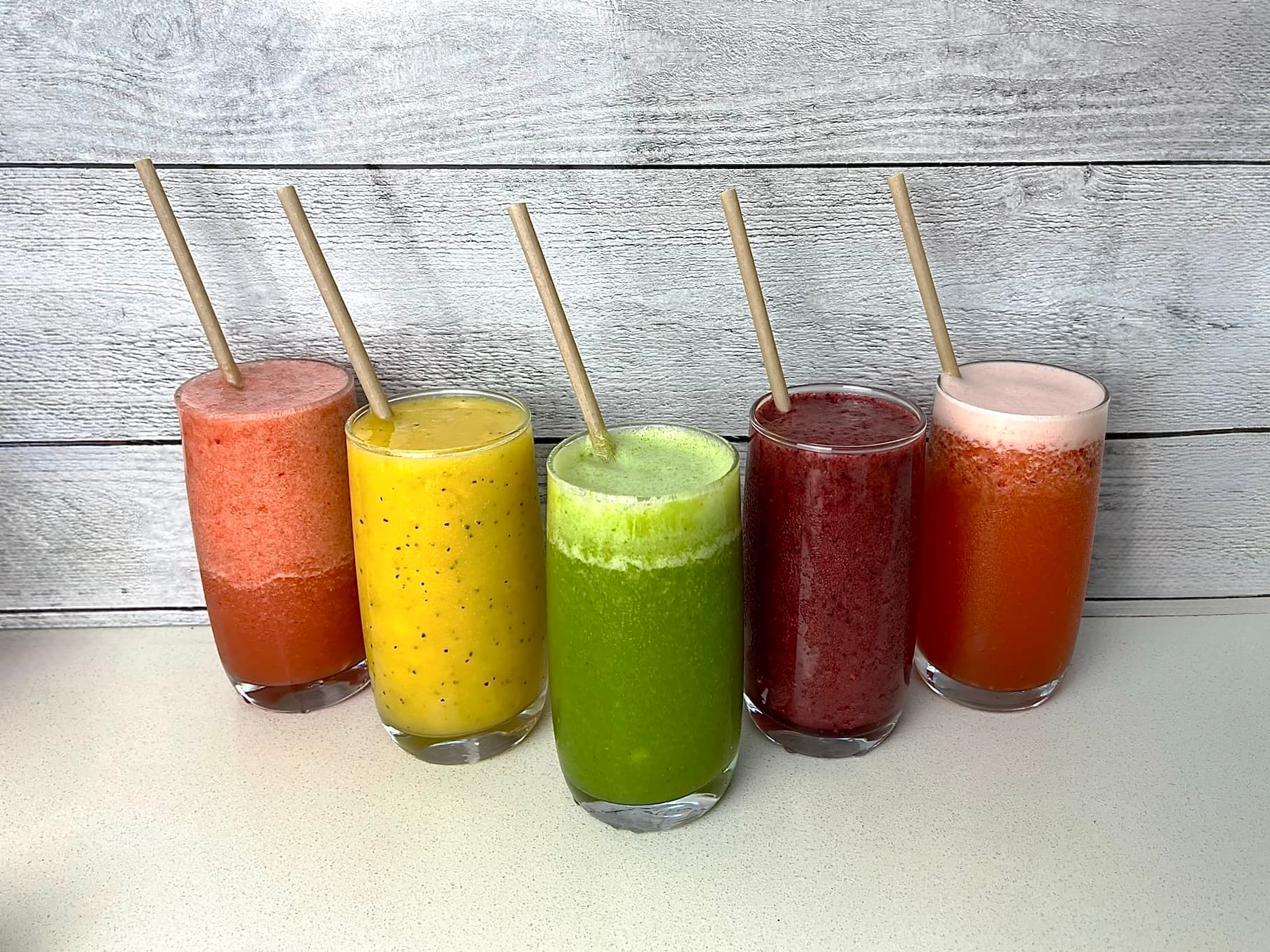 A colourful lineup of different smoothie flavours in clear cups.